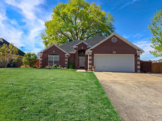 Single-story brick house with a garage and green lawn under a bright blue sky.