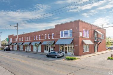 Brick building with multiple storefronts and gray awnings along a street.