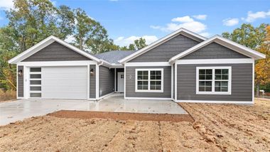 Gray house with white trim, a two-car garage, and a concrete driveway on a sunny day.