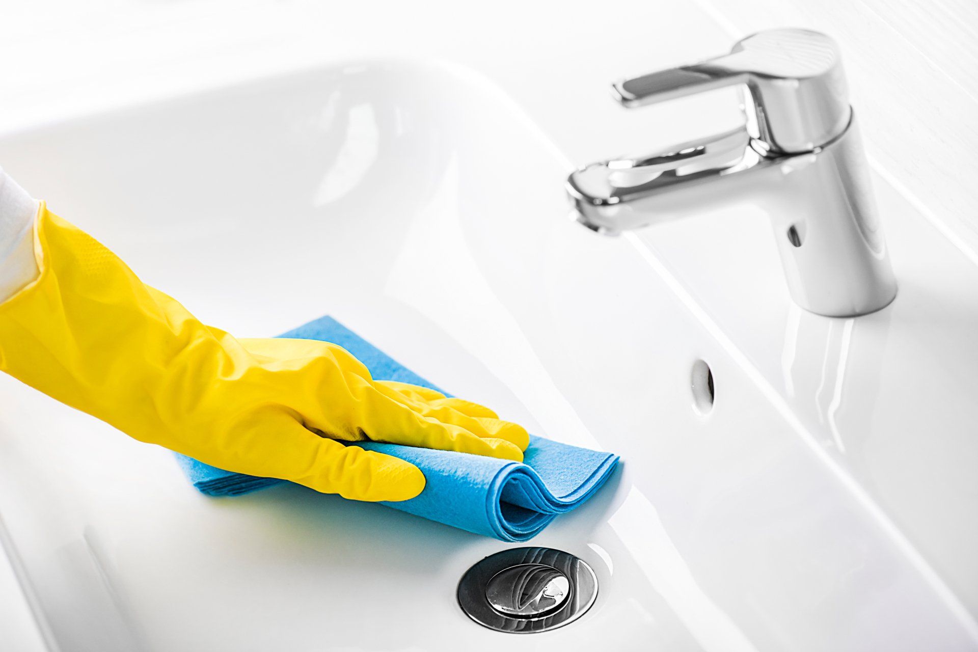 Picture of a basin being cleaned with a left hand yellow glove on and blue sponge