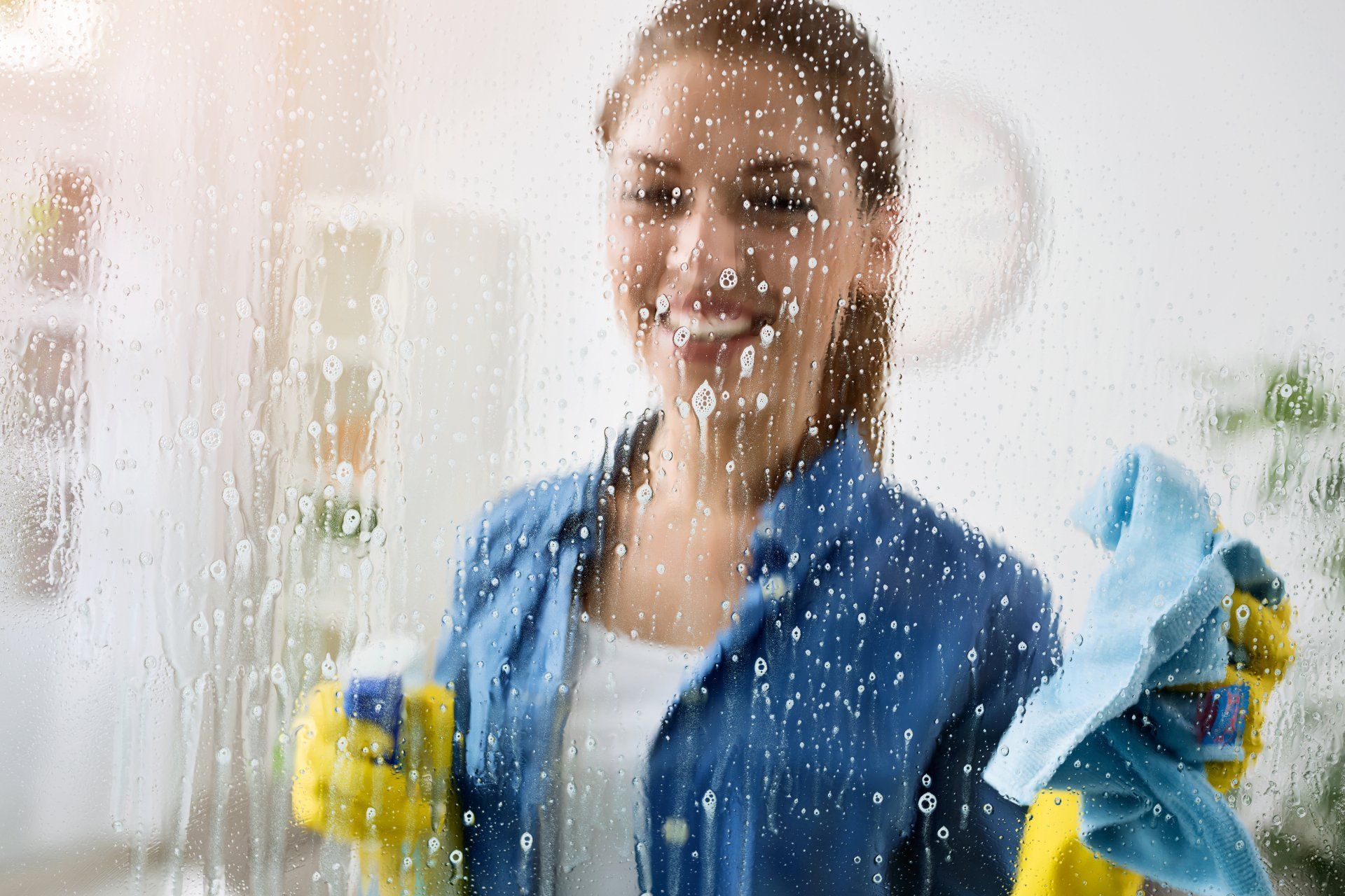 A series of 4 images including a kitchen are with white tiles  chopping board on the bench and some cleaning products, a cleaning lady wiping a shower screen, a steam cleaner running over some carpet and a person wiping down a toilet.