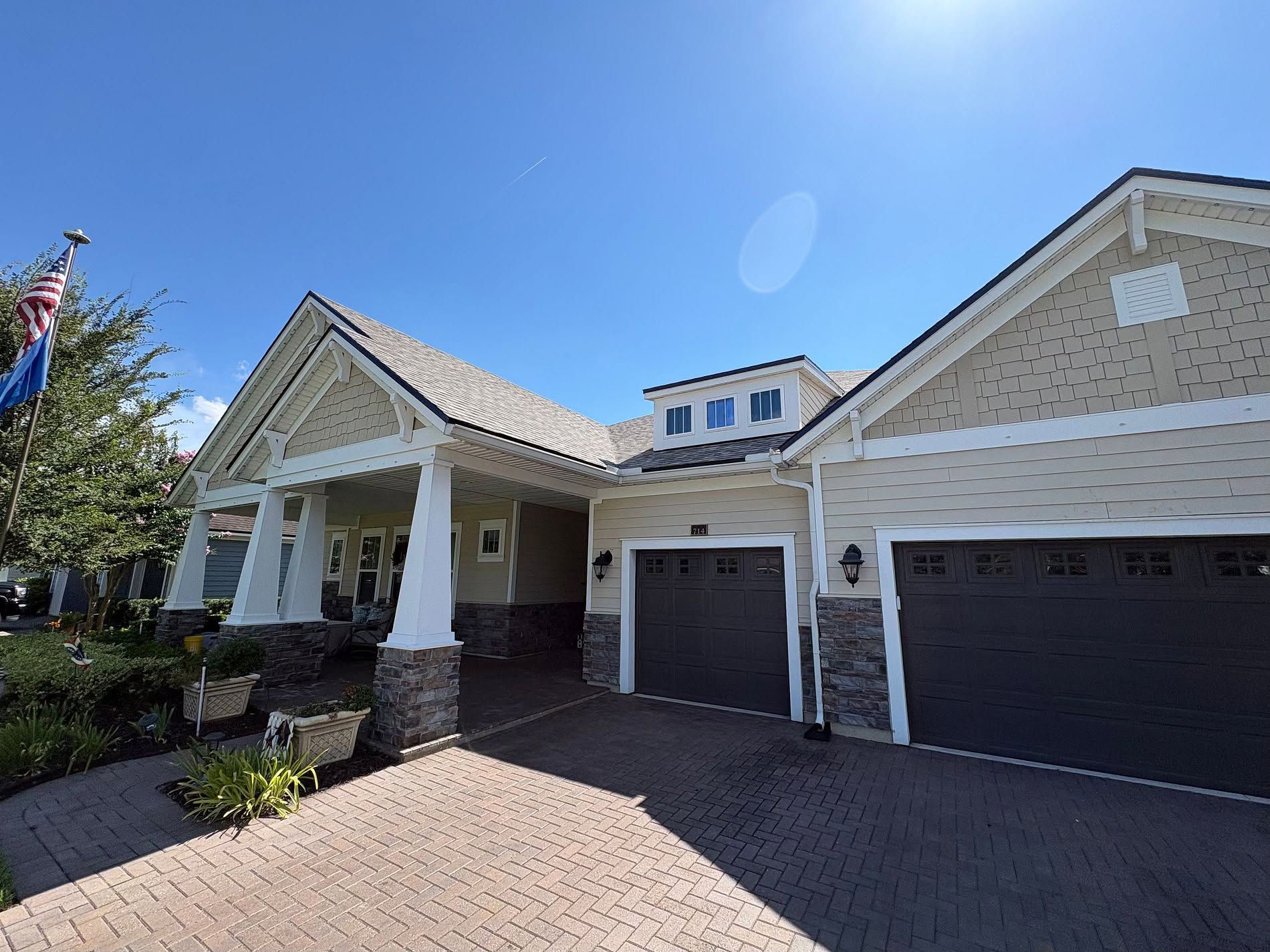 Large beige suburban house with columns, double garage, and brick driveway under a bright blue sky