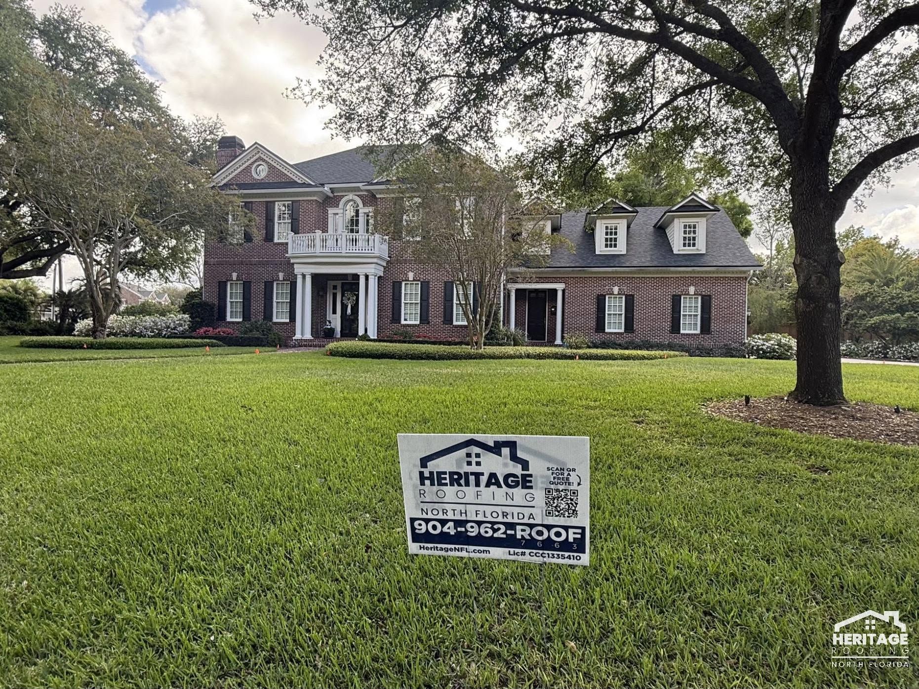 Historic brick mansion with white columns behind a lawn and a heritage sign in front