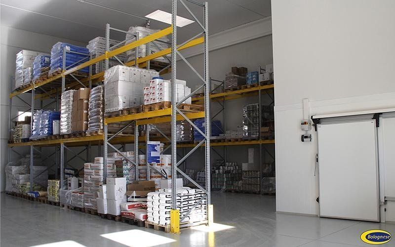 Interno di un magazzino con scaffali pieni di merci confezionate, vicino a una porta scorrevole.