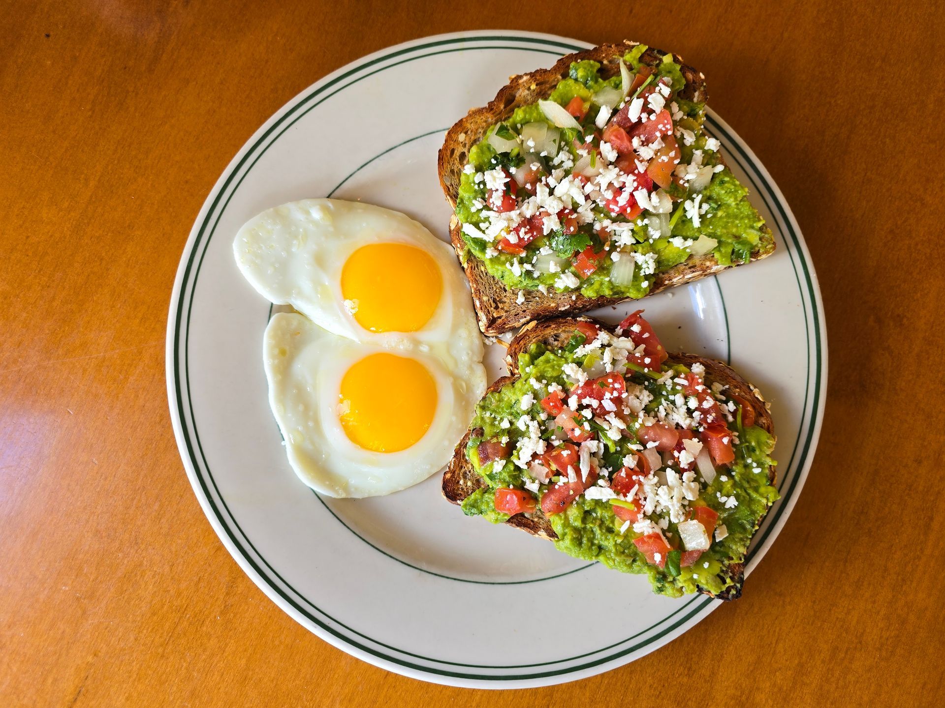 Plate of avocado toast topped with feta, and two sunny-side-up eggs.
