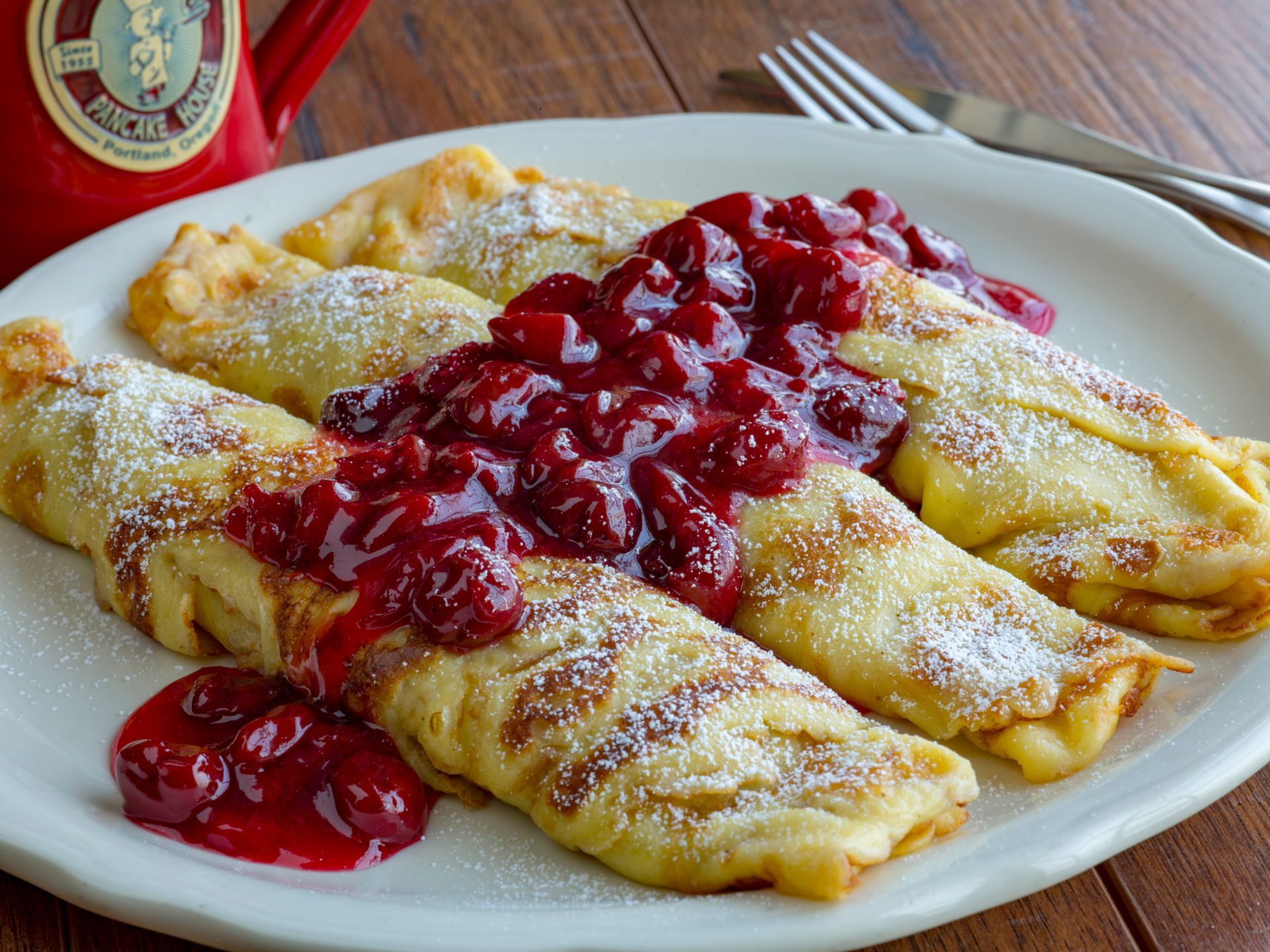 Crepes with cherry topping dusted with powdered sugar on a white plate.