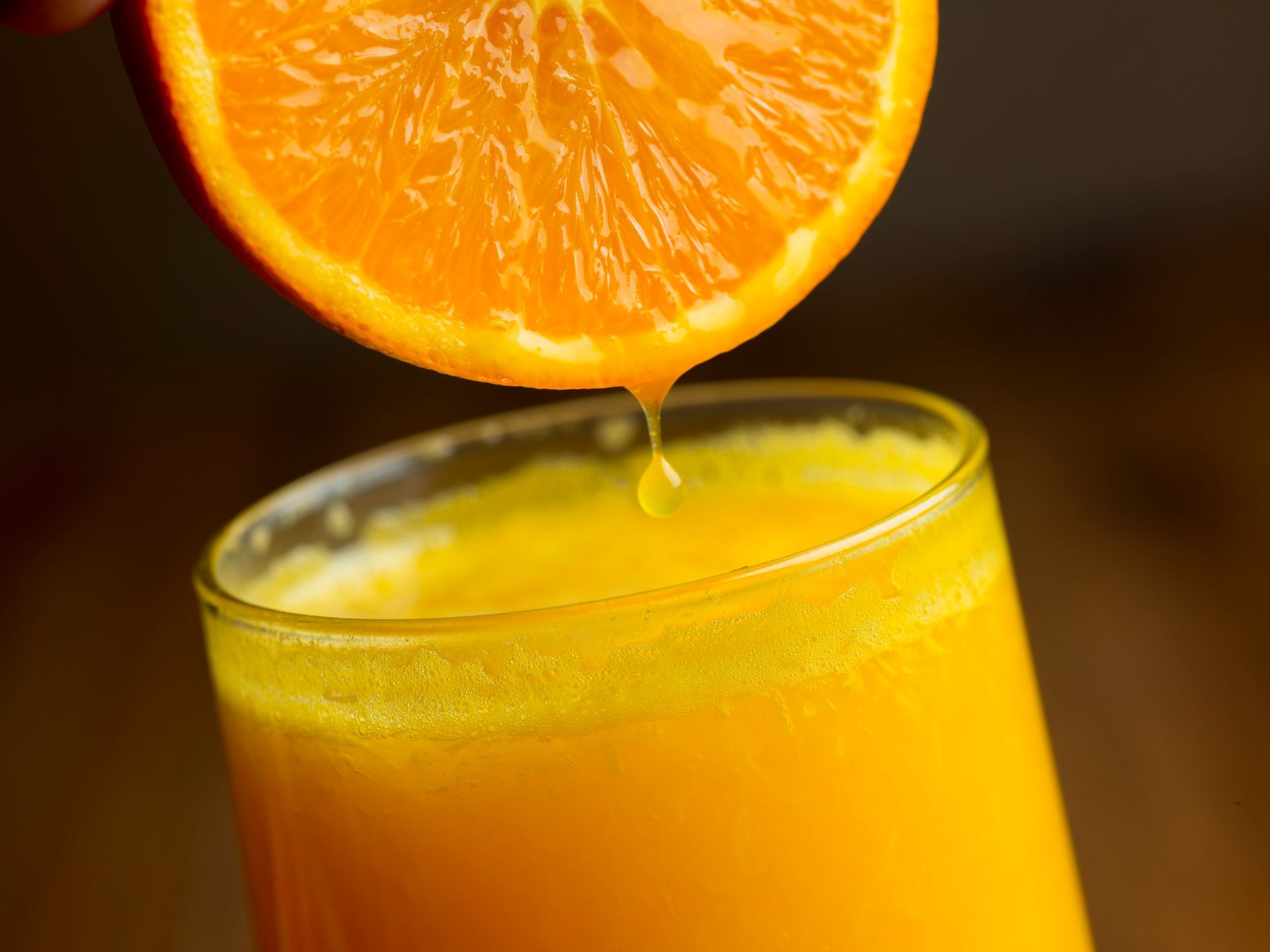 Orange slice dripping juice into a glass of orange juice.