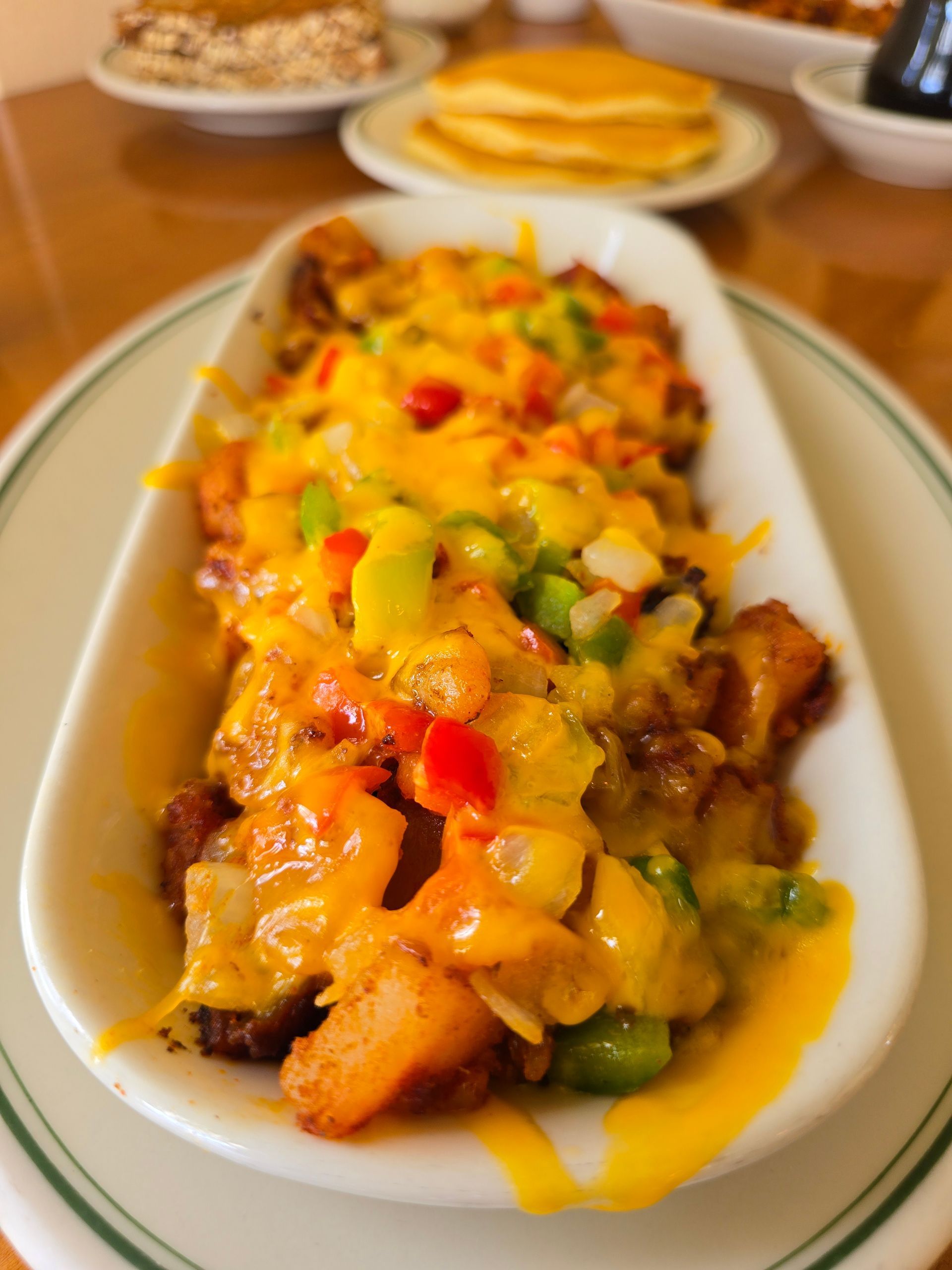 Loaded potatoes with melted yellow cheese, peppers, and onions in a white dish.