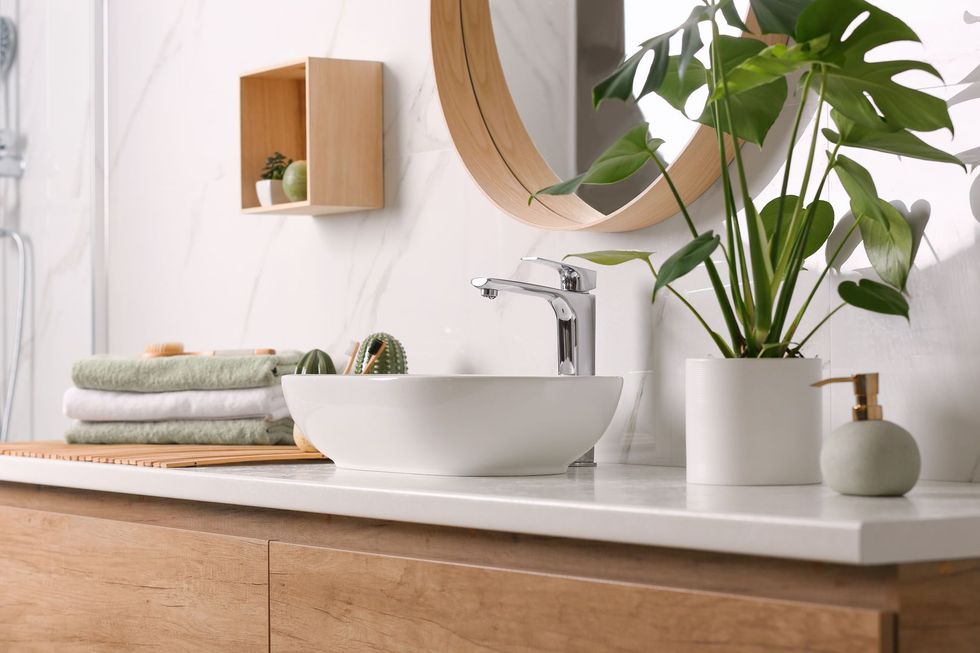 Une salle de bain avec lavabo, miroir, plante et serviettes.