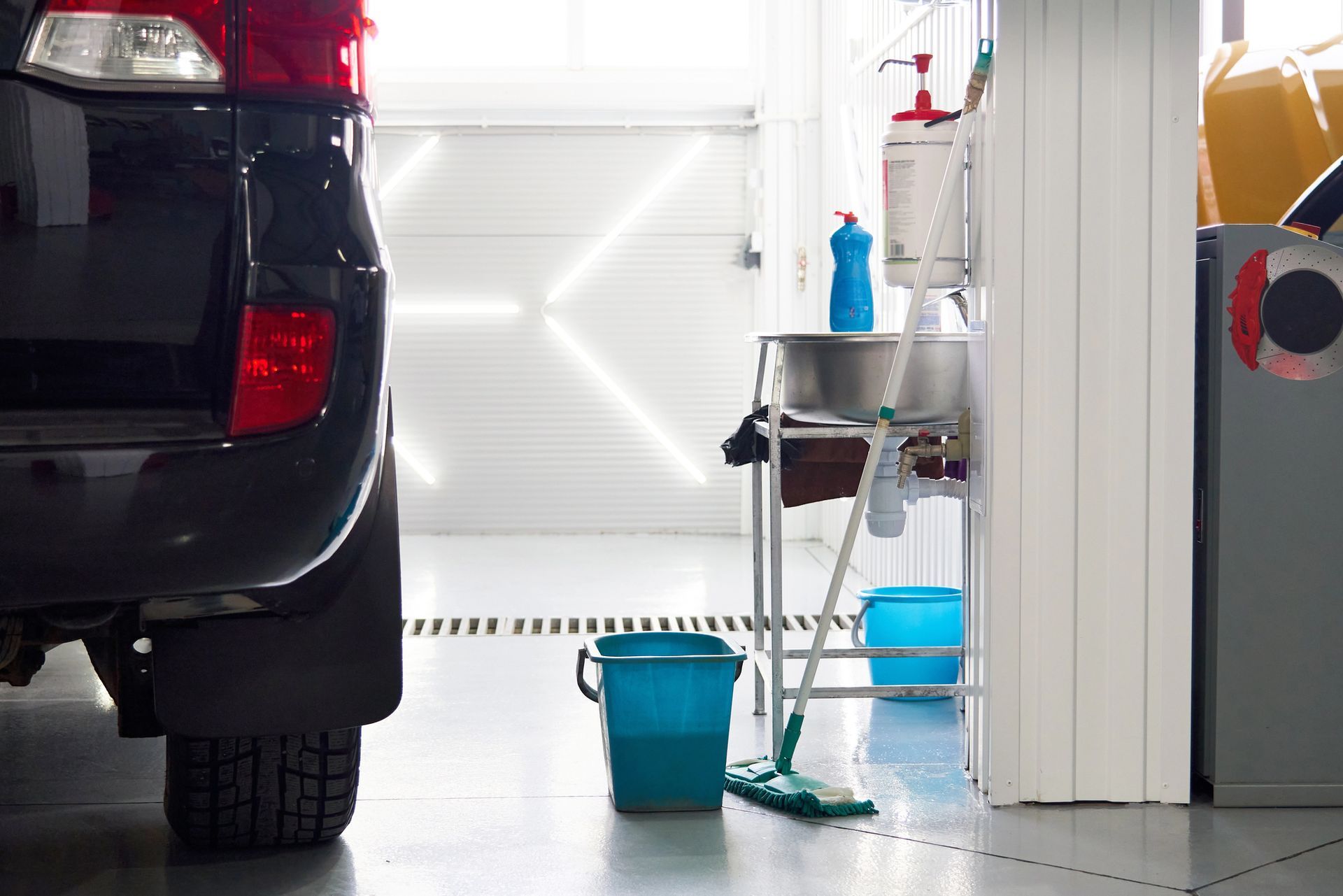 Black SUV in a car wash, cleaning supplies, blue buckets, and a white garage door.