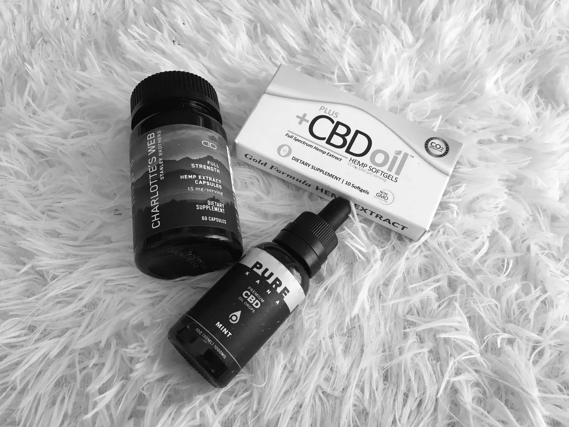 Three CBD oil bottles and a CBDoff box arranged on a white, shaggy textured surface.