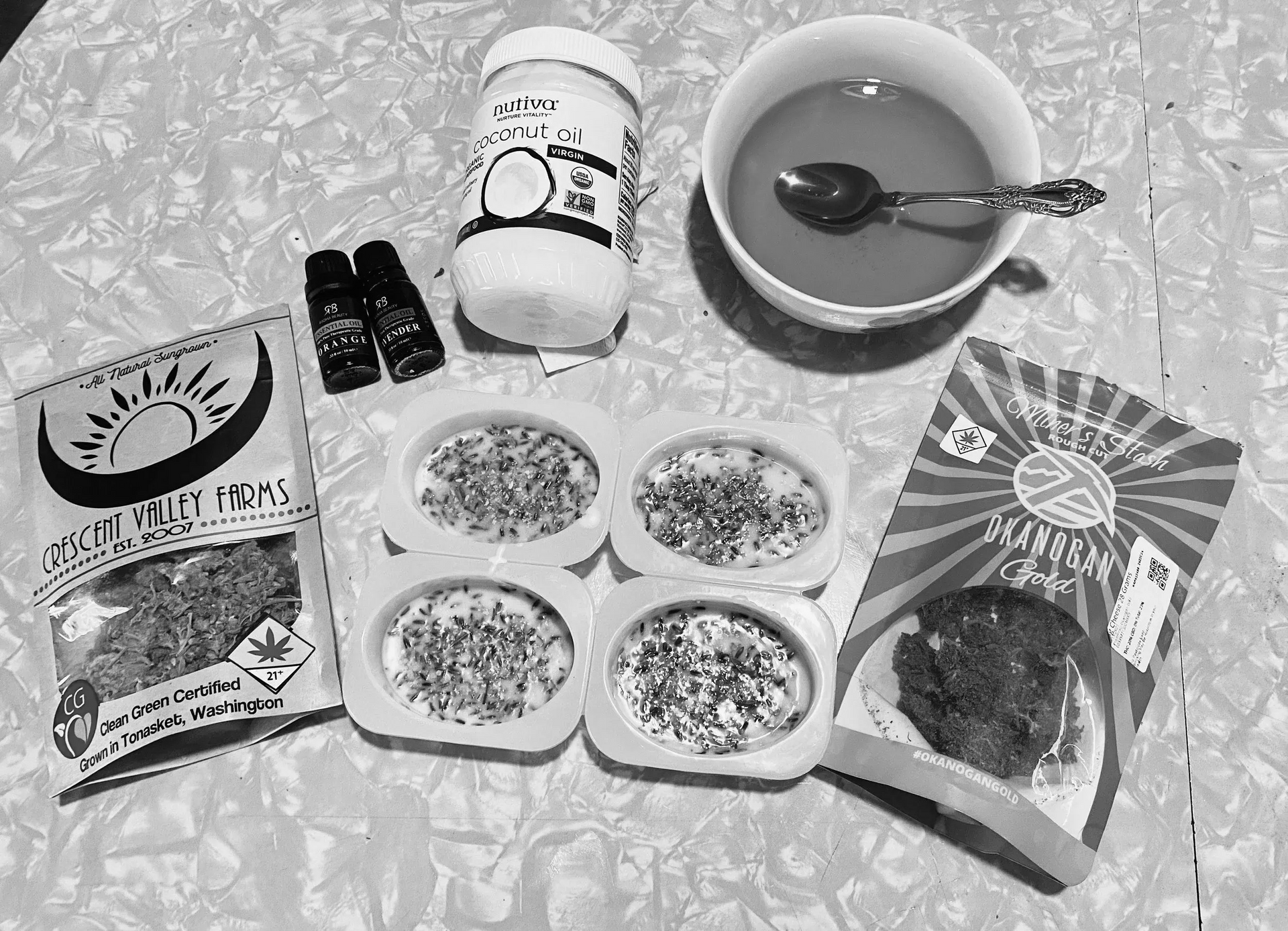 A flat lay showing coconut oil, a tea cup, two small vials, a cannabis product bag, and four silicone soap molds.
