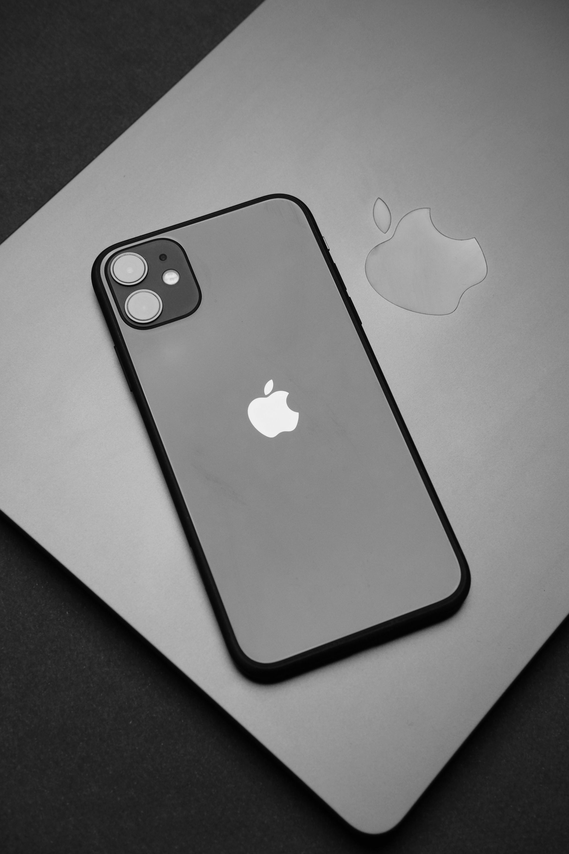 A black iPhone 11 with its dual-camera array resting on top of a closed silver Apple laptop.