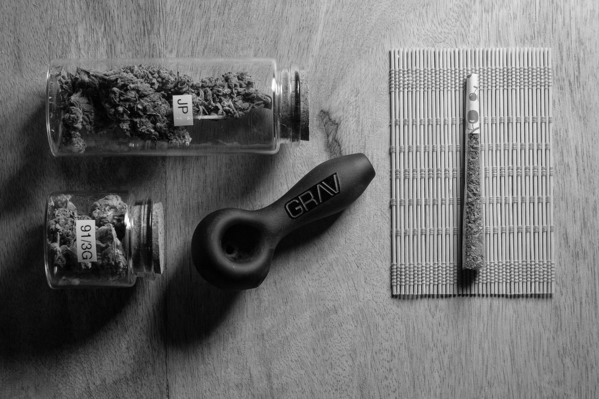 Two small glass jars containing cannabis, a black GRAV pipe, and a metal lighter on a bamboo rolling mat.