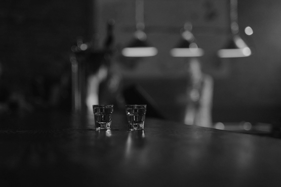 Two small shot glasses sitting on a bar counter in a dimly lit, out-of-focus lounge setting.