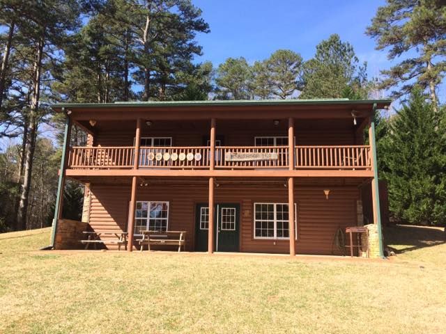 Two-story brown cabin with a green roof and balconies, in a grassy area with trees.