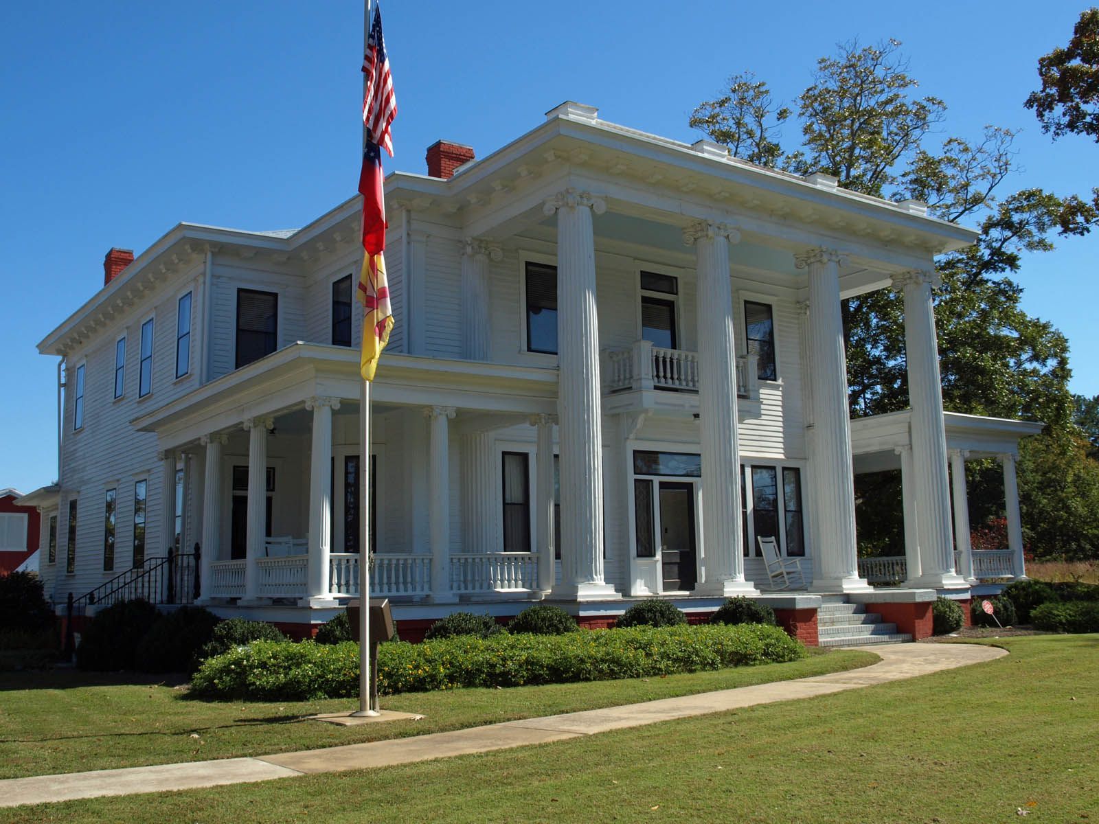 White two-story house with columns, porch, and American flag on sunny day. Commercial and residential plumbing in Braselton.