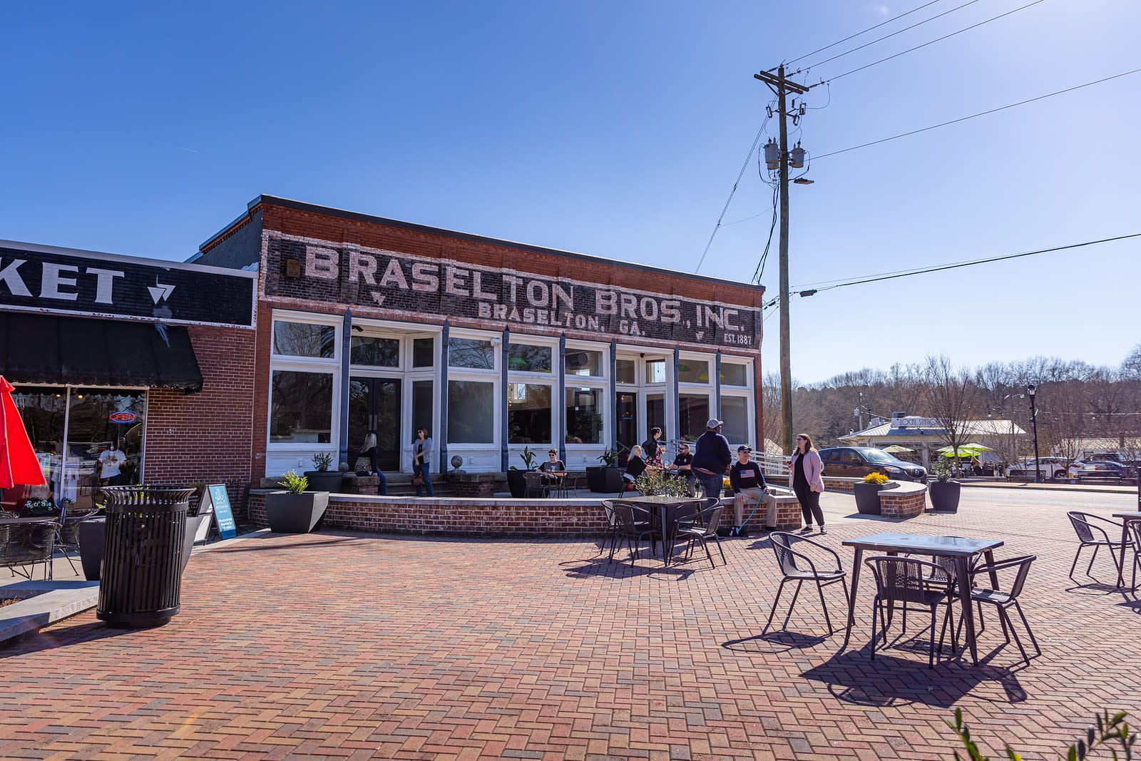 Braselton Bro’s Inc. building with outdoor seating on a brick patio. Blue sky and sunny day. Store plumbers in Braselton GA.