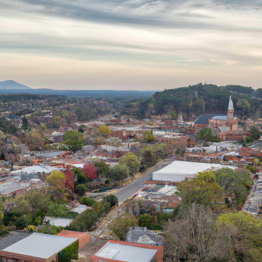 Aerial view of a town with buildings, roads, trees, and a tall church steeple under a cloudy sky. Plumbing company in Dacula.