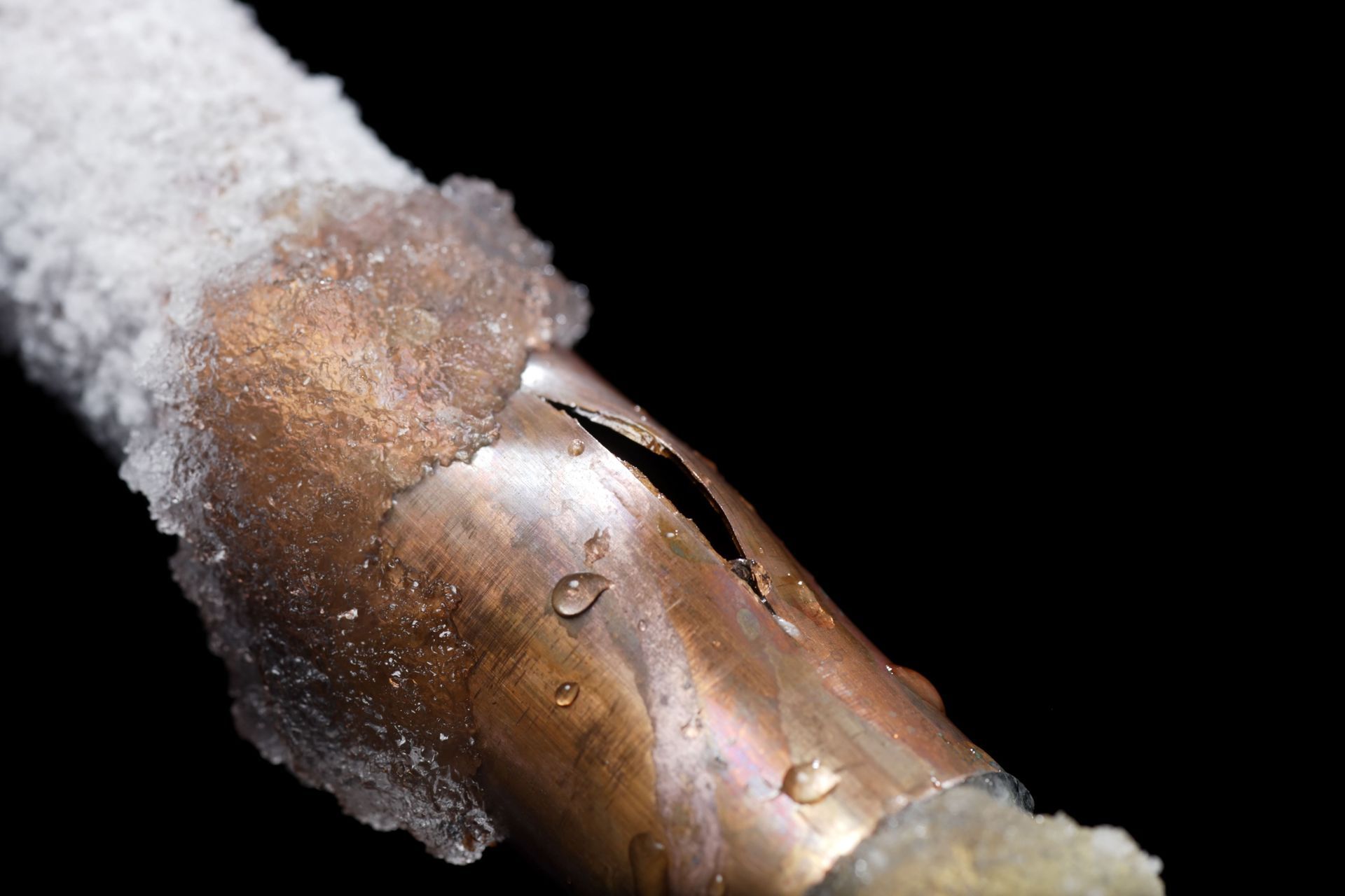 Cracked copper pipe with ice formation, isolated against black background. Protecting your home during overnight freeze.