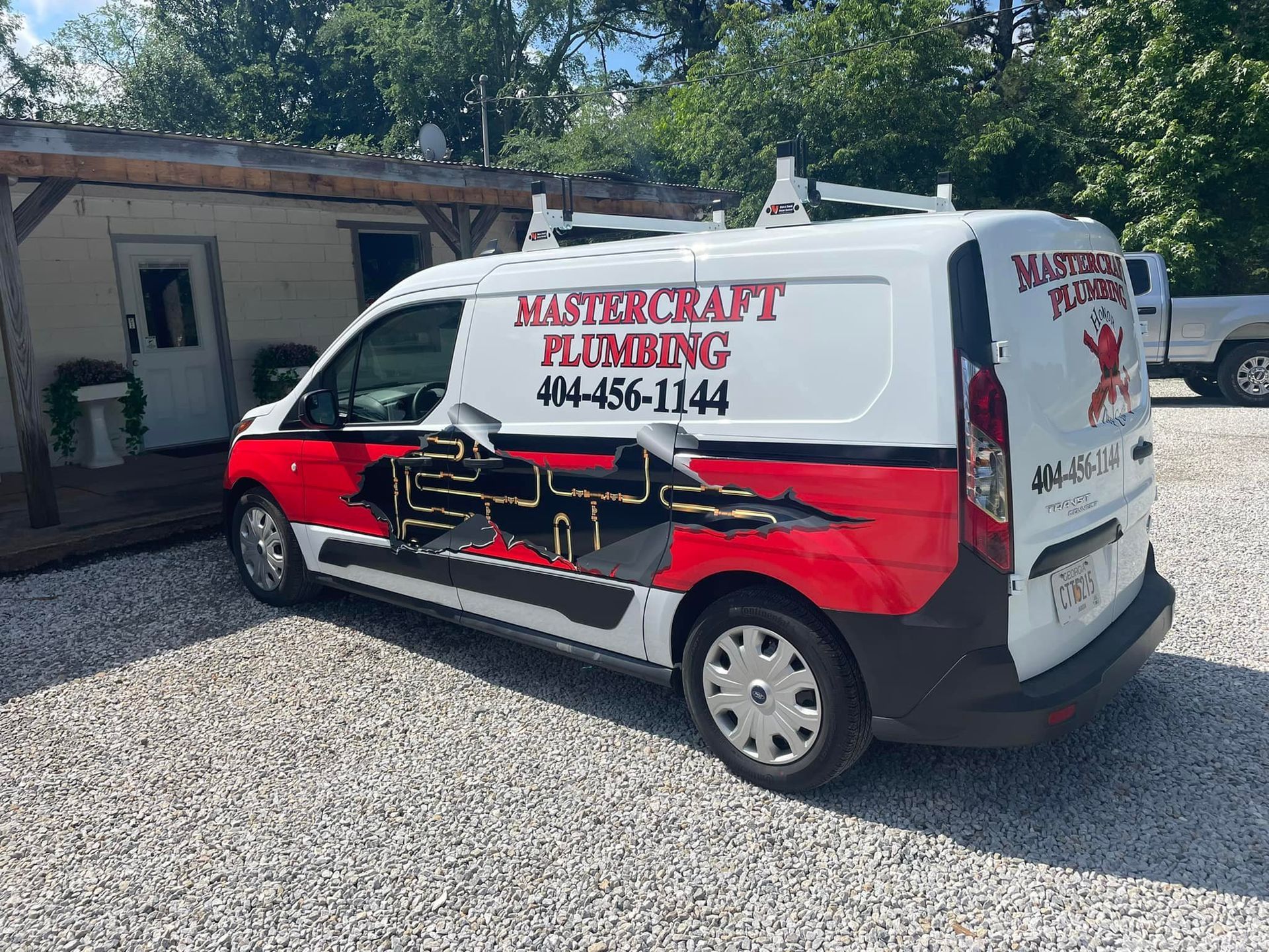 White and red Mastercraft Plumbing van parked on gravel, with a business logo and phone number.
