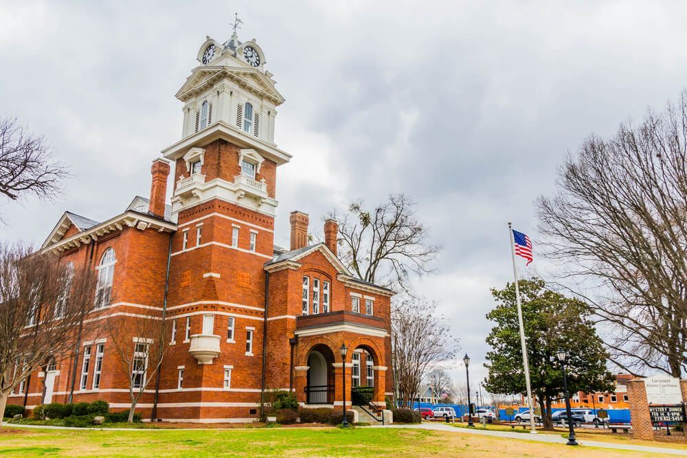 Brick courthouse building with clock tower and American flag on cloudy day. Commercial and residential plumber Lawrenceville.