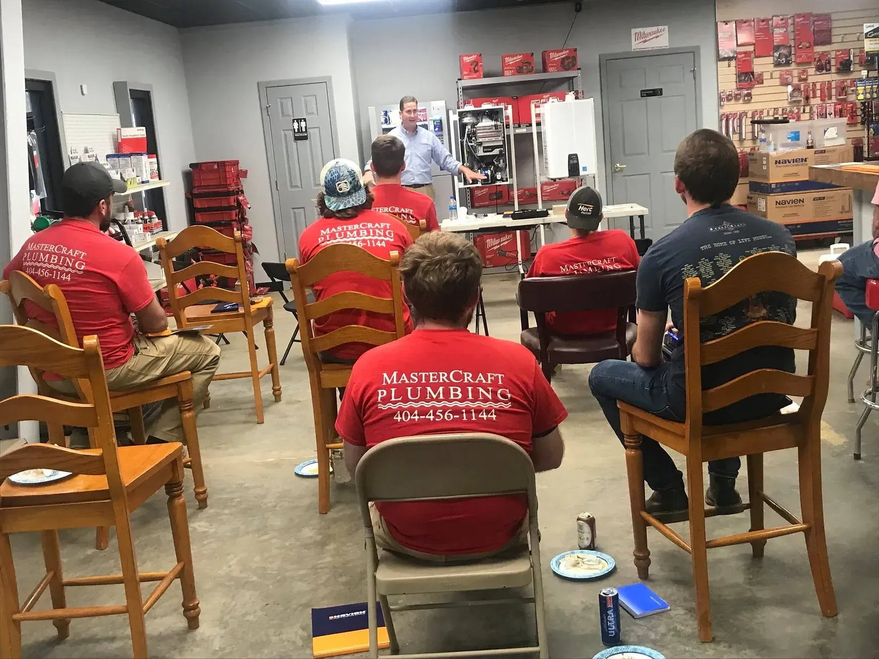 A group of people in red shirts listen to a presentation in a workshop setting.