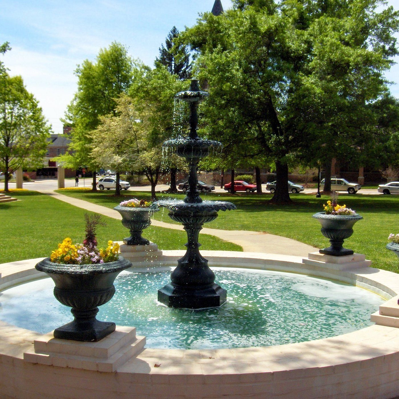 Fountain in a park with surrounding flower pots, trees, and parked cars. Commercial contractor plumbers in Gainesville GA.
