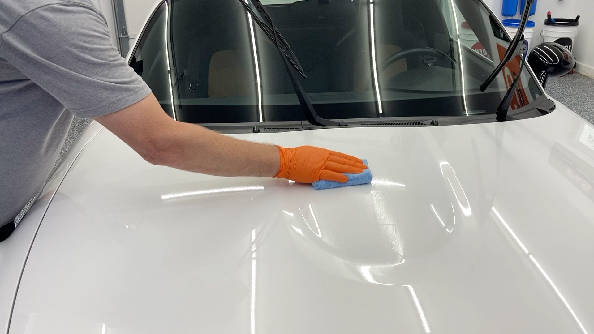 A man is cleaning the hood of a white car.