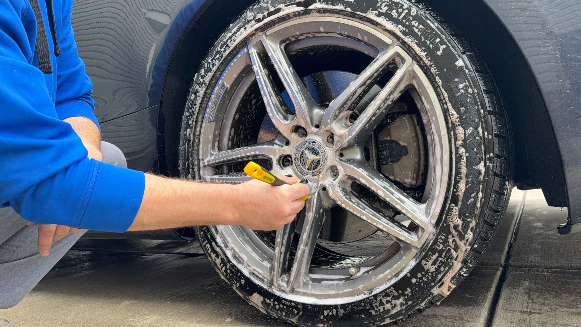 A person is cleaning a car wheel with a brush.