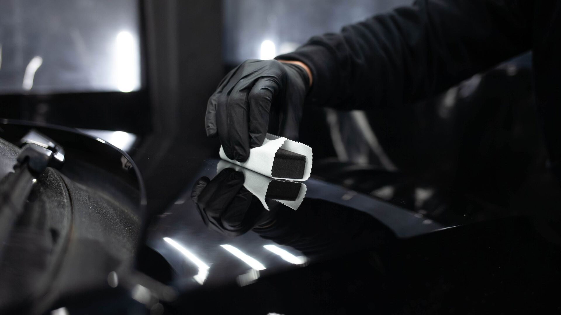 A person wearing black gloves is cleaning a car with a brush.