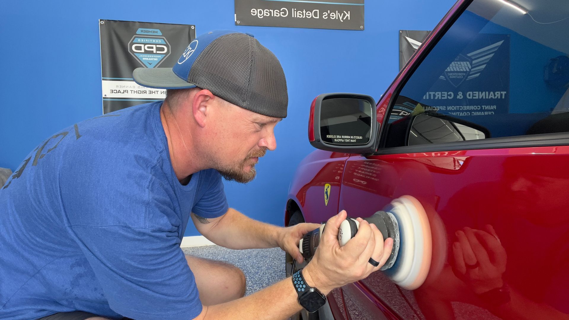 A man is polishing a red car with a polisher.