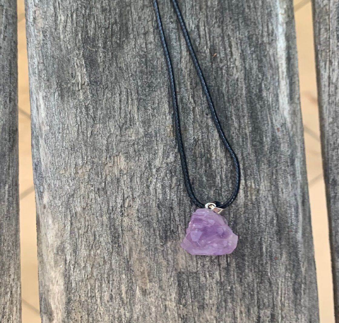 A necklace with a purple stone pendant is sitting on a wooden chair.