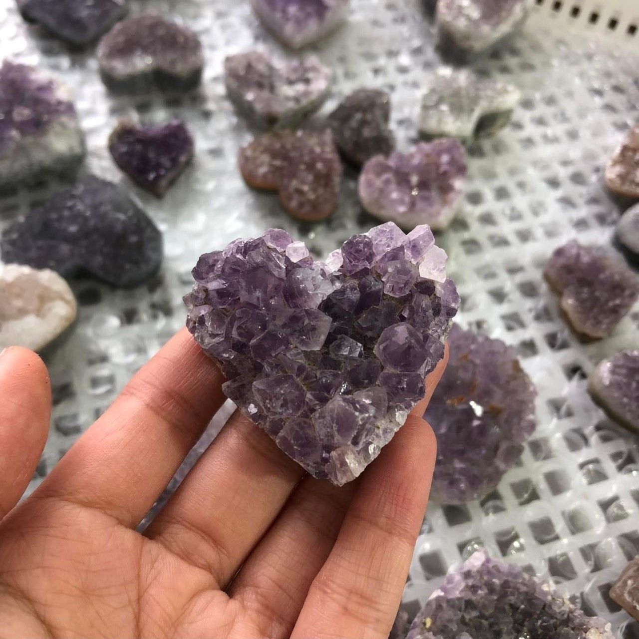 A person is holding a heart shaped amethyst in their hand.