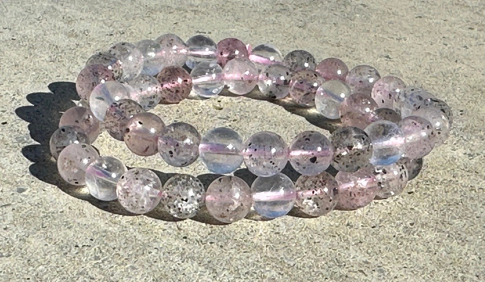 A bracelet made of pink and clear beads is sitting on a concrete surface.