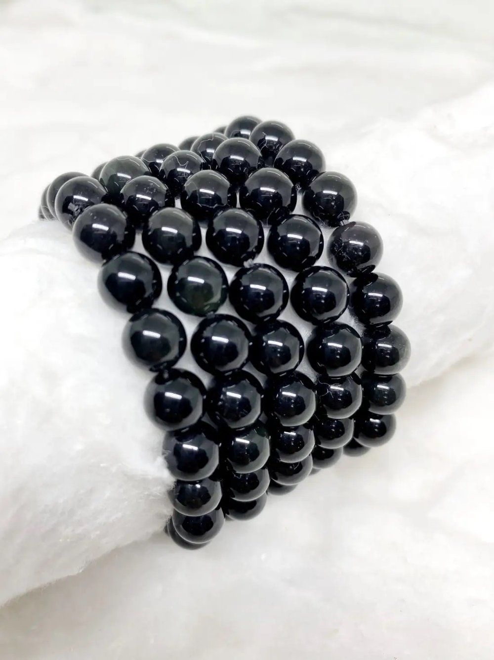 A bracelet made of black beads is sitting on a white cloth.