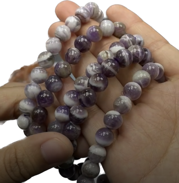 A bracelet made of purple beads is sitting on a table next to a palm tree leaf.