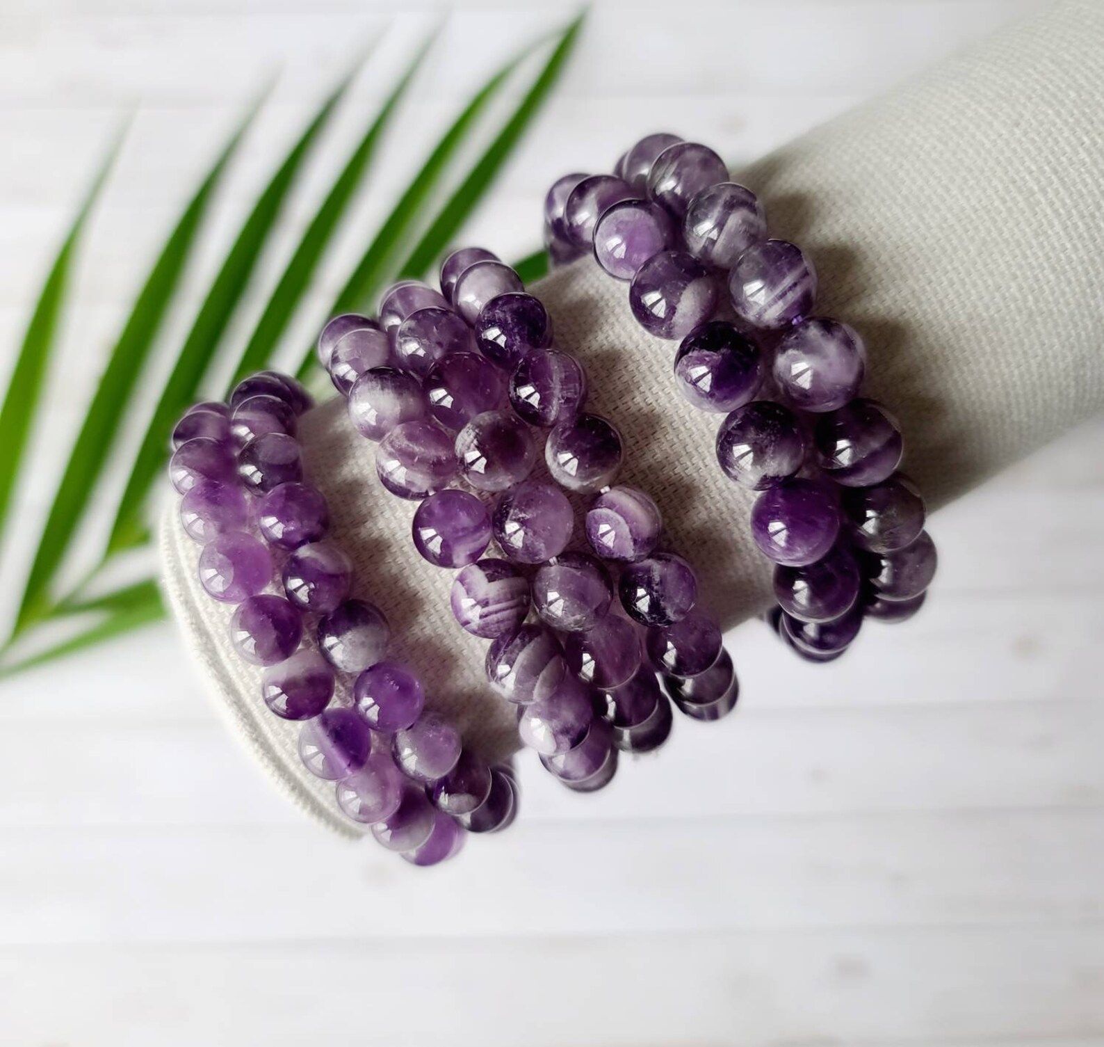 A bracelet made of purple beads is sitting on a table next to a palm tree leaf.