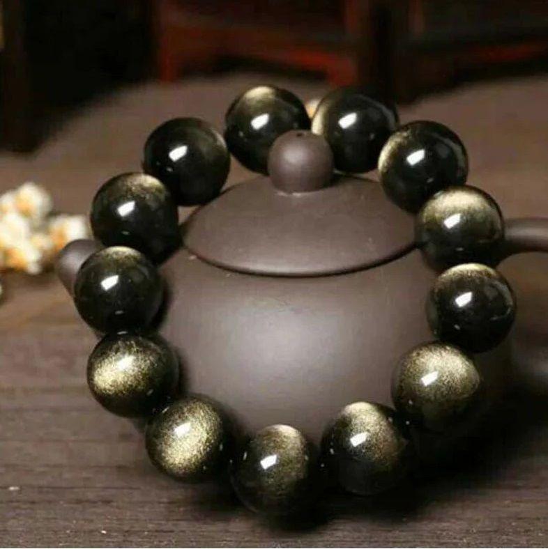 A close up of a bracelet with black and gold beads on a table.