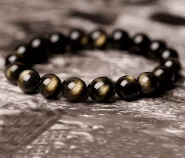 A close up of a bracelet with black and gold beads on a table.