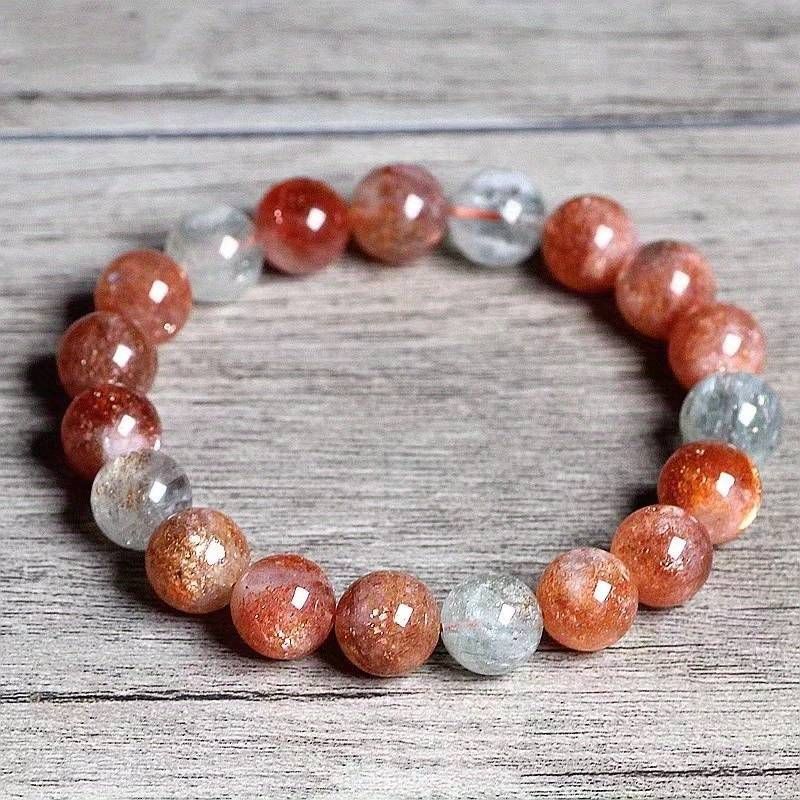 A bracelet made of red and clear beads is sitting on a wooden table.