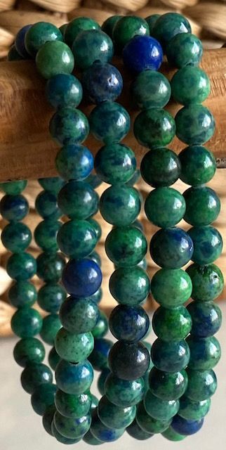 A bracelet made of green and blue beads is sitting on a wooden table.