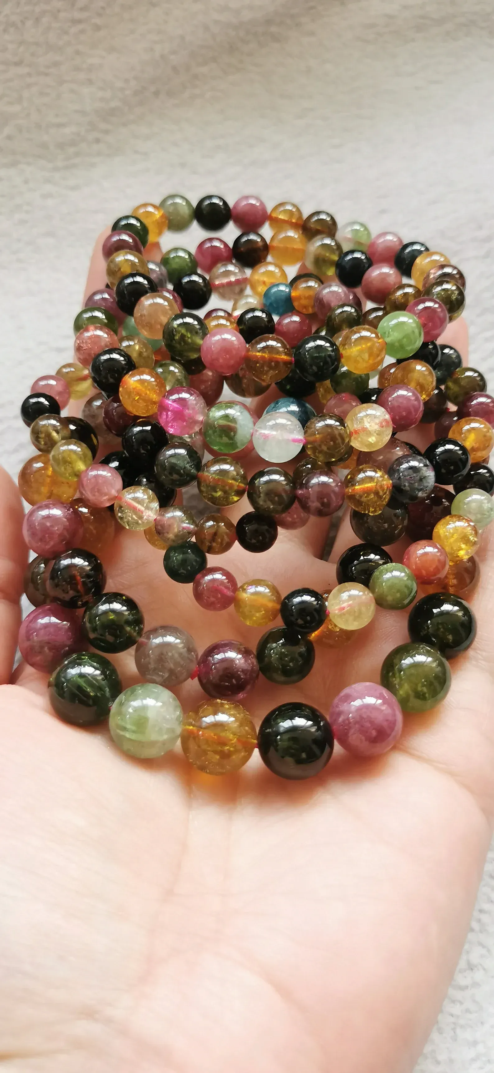 A person is holding a necklace of colorful beads in their hand.