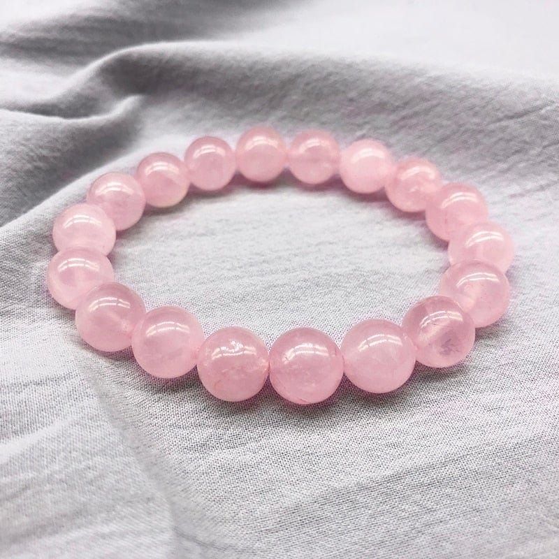 A bracelet made of pink beads is sitting on a white cloth.