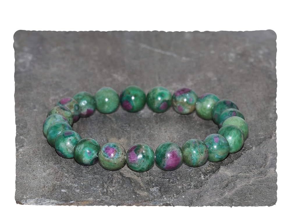 A bracelet made of green and pink beads is sitting on a rock.