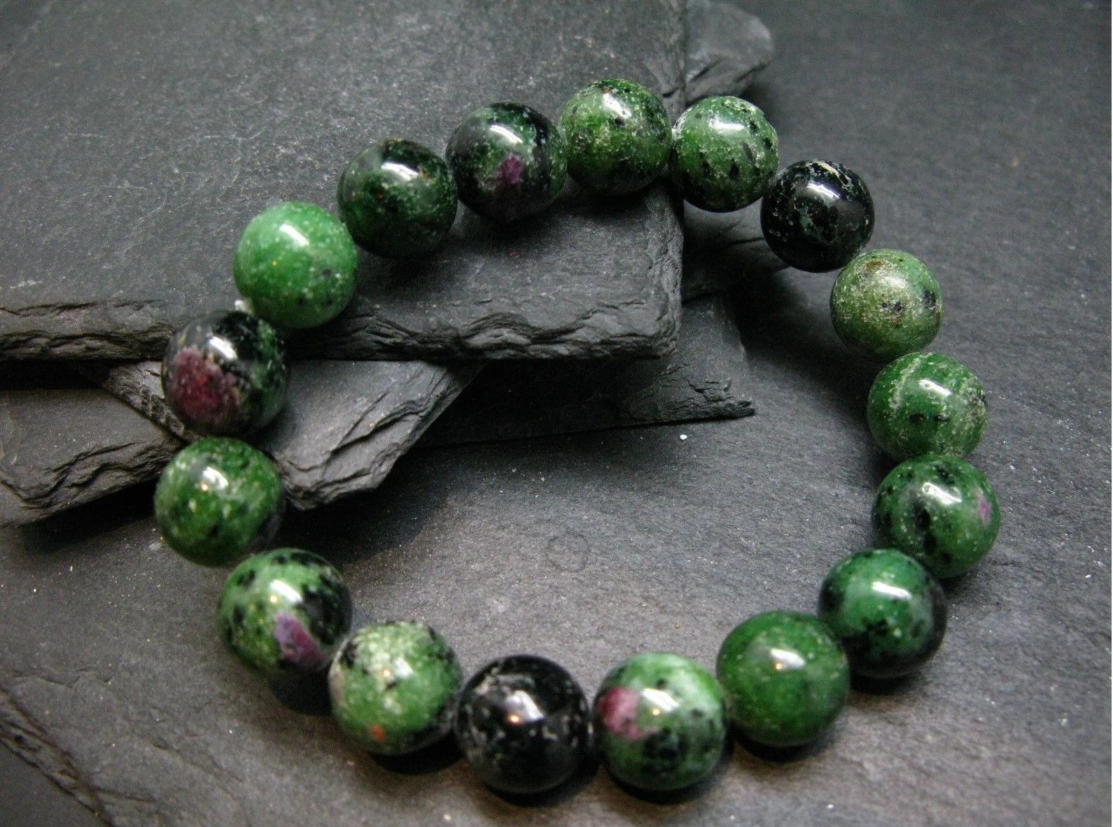 A bracelet made of green and pink beads is sitting on a rock.
