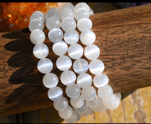 A bracelet made of white beads is sitting on a wooden stick