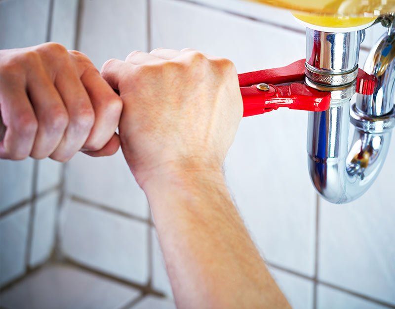 Plumber hands holding wrench for cleaning a sink in bathroom
