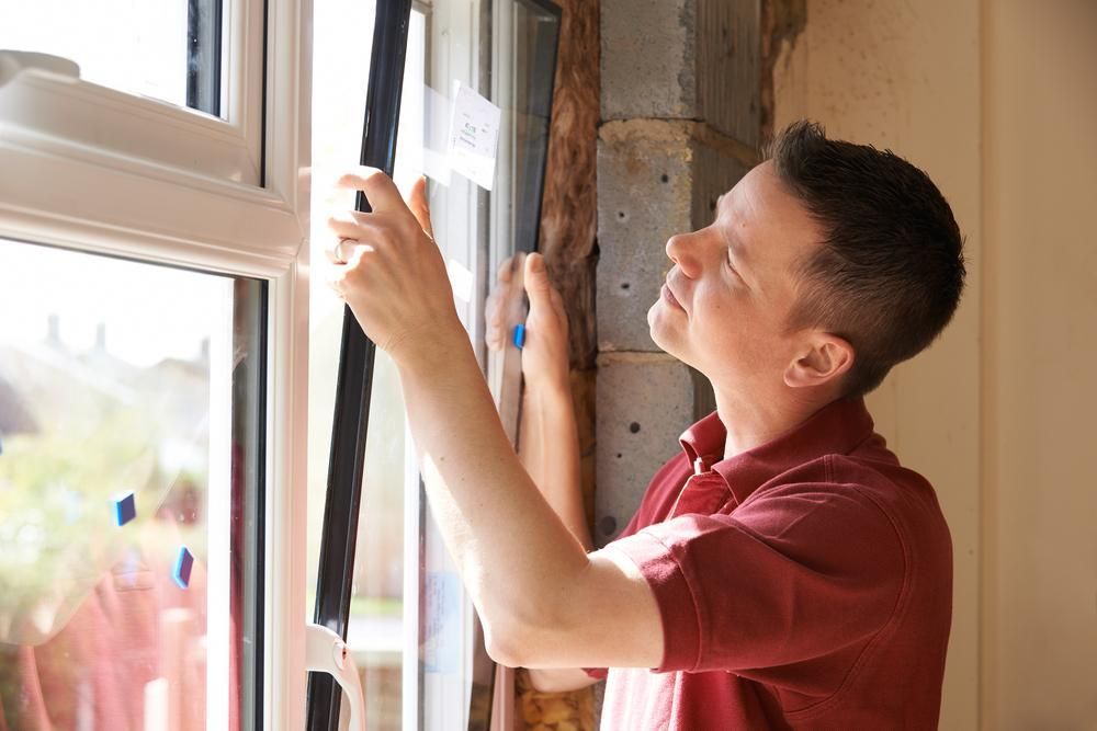 A Man in a Red Shirt is Installing a Window — Headlands Glass in Brunswick Heads, NSW