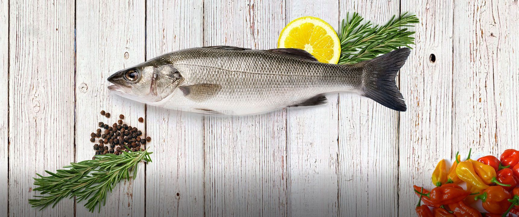 A fish is sitting on a wooden table next to a lemon slice.